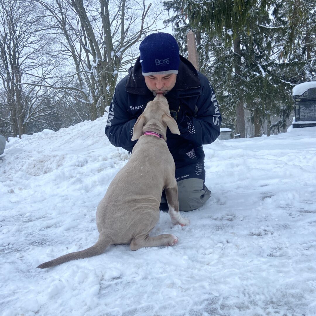 A person kneeling down in the snow petting a dog.