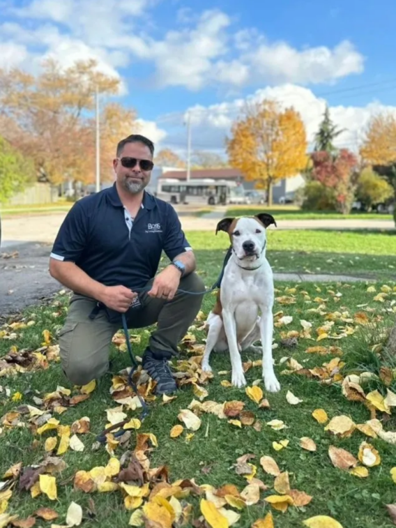 Man in sunglasses crouching with dog among leaves
